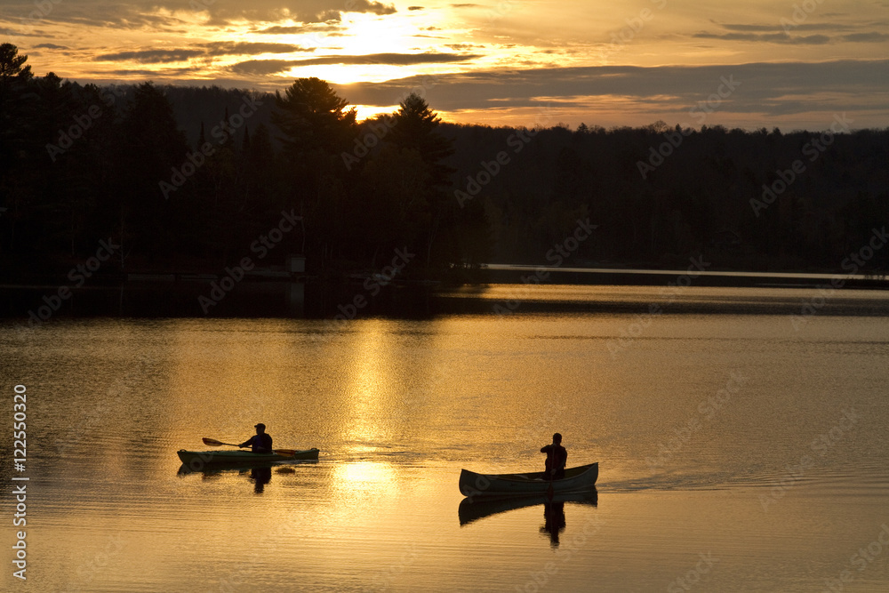 Two men paddle canoe and kayak on Oxtongue Lake at sunrise, Muskoka, Ontario, Canada. Two men paddle canoe and kayak on Oxtongue Lake at sunrise, Muskoka, Ontario, Canada.