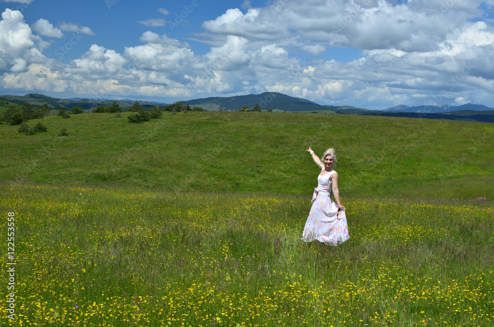 Woman standing in a meadow and showing towards hills Woman standing in a meadow and showing towards hills