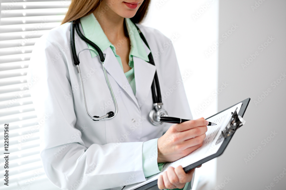 Female doctor filling up medical history standing near the window in hospital