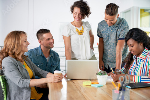 Multi ethnic group of succesful creative business people using a laptop during candid meeting photo