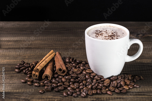 cup of coffee with coffee beans and cinnamon on wooden table. Image with copy space