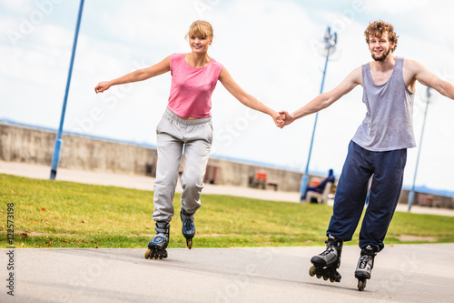 Young couple rollerblading in park holding hands.