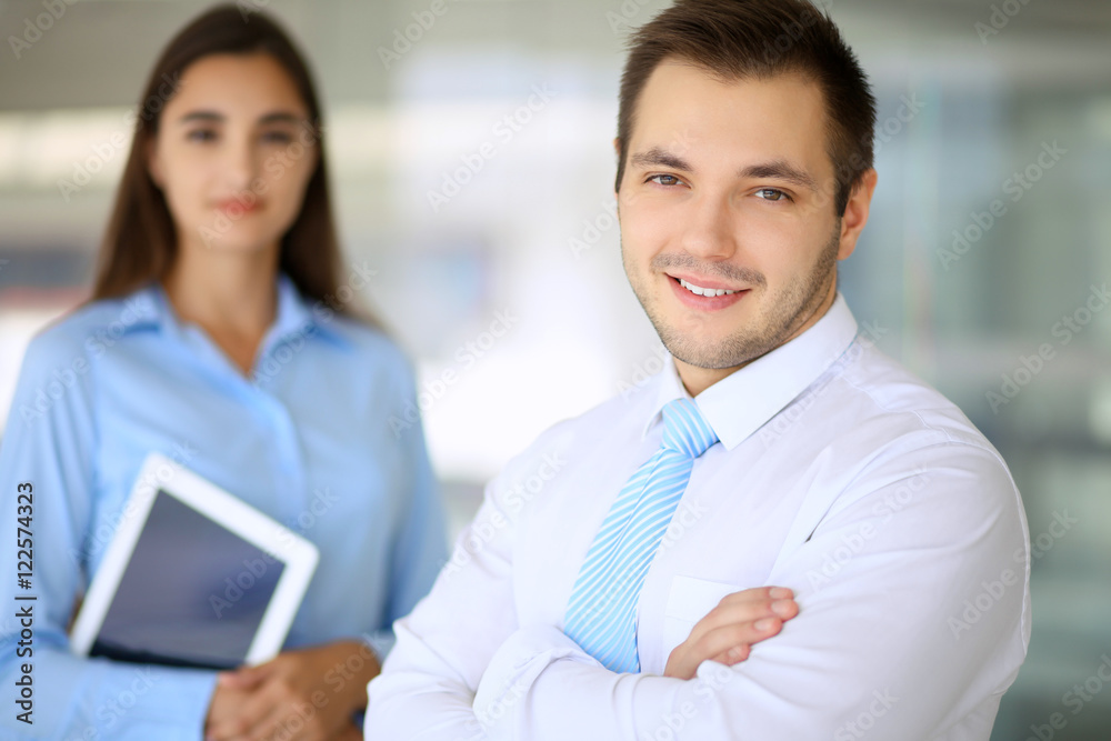Smiling businessman in office with colleagues in the background Smiling businessman in office with colleagues in the background