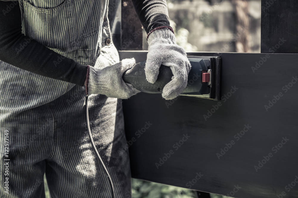 hands with gloves holding sander machine, polishing black wood surface, saturated color tone