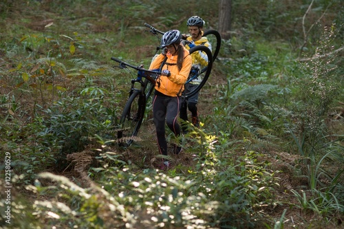 Biker couple carrying their mountain bike and walking in forest