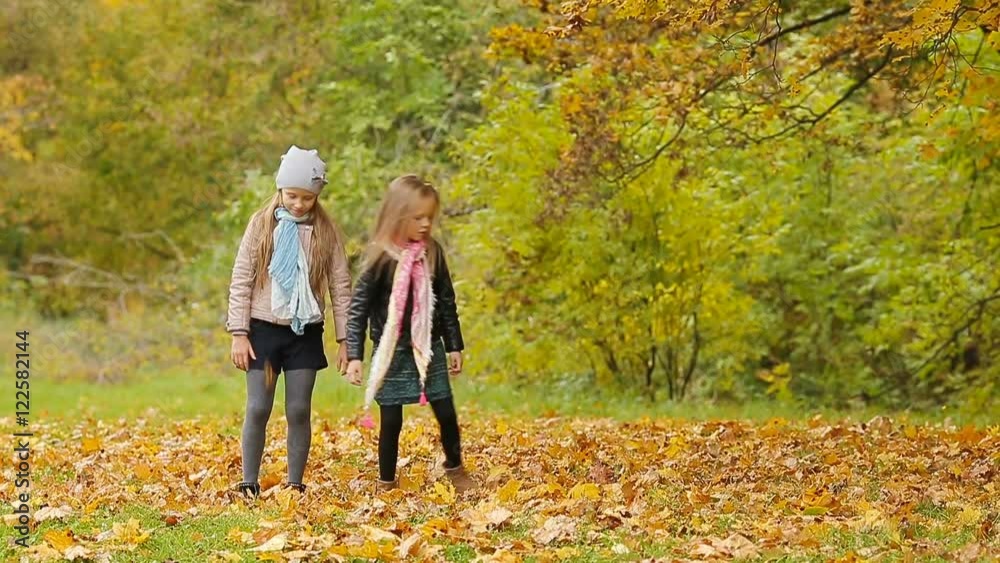 Little adorable girls having fun with leaves at warm day in autumn park outdoors Little adorable girls having fun with leaves at warm day in autumn park outdoors