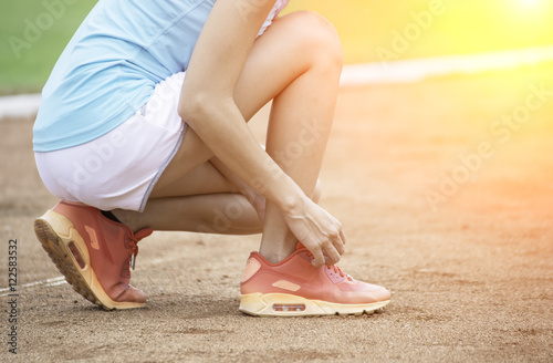 Young woman tying laces of running shoes before training
