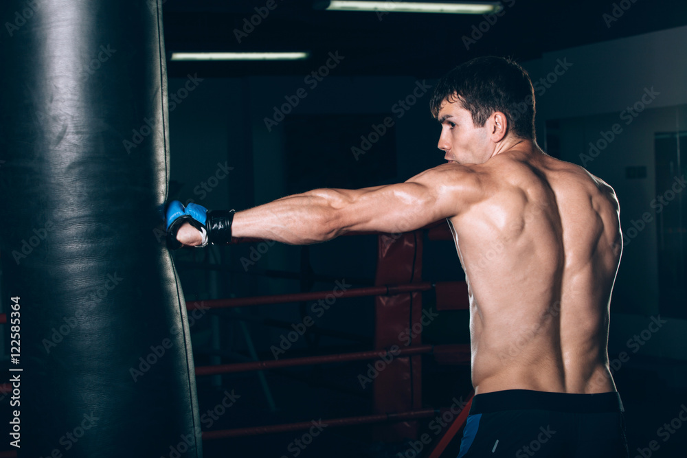 Young Male boxer using a punching bag in gym.