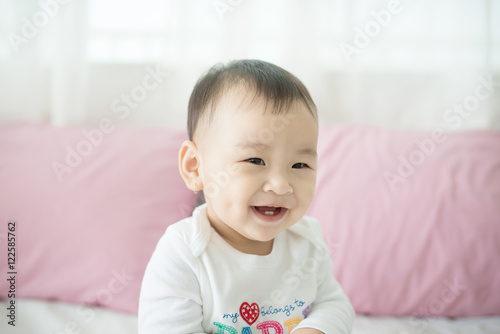 Lovely asian baby girl sitting on bed at her room.