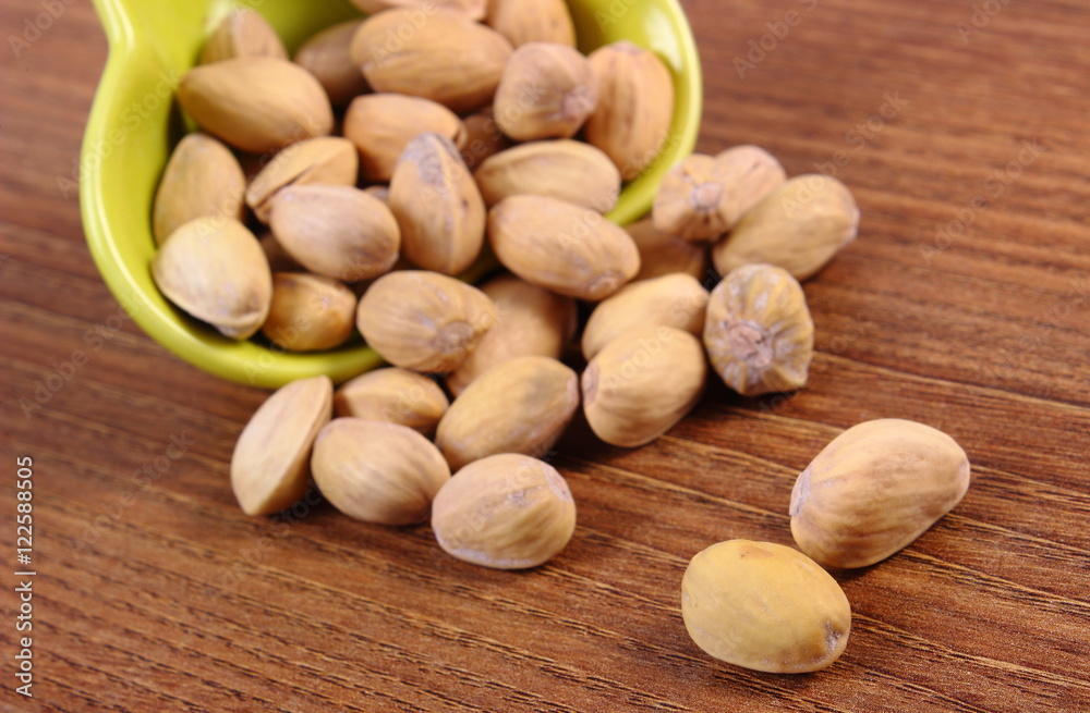 Obraz premium Pistachio nuts in bowl on wooden table, healthy eating