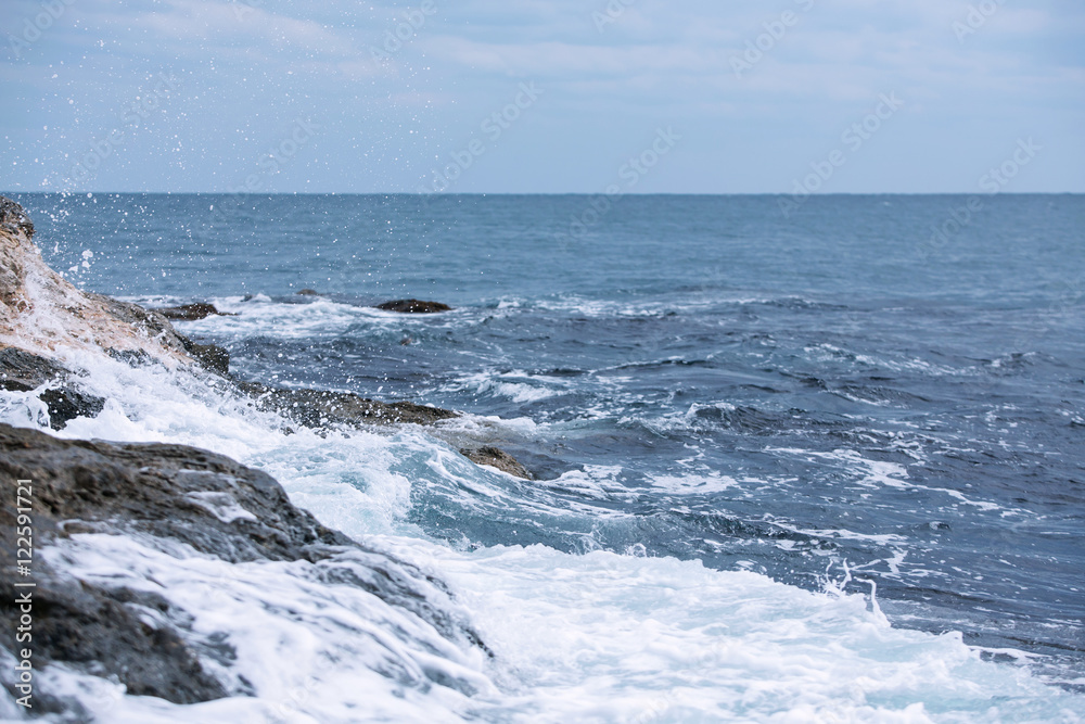 Deep dark blue sea waves breaking on a rocks forming a sea foam.