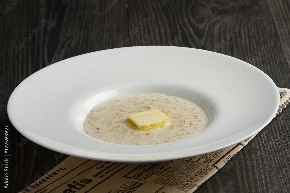 Plate of liquid oatmeal with piece of butter on wooden table Plate of liquid oatmeal with piece of butter on wooden table