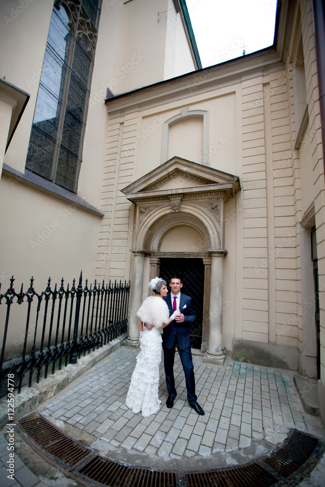 Stylish wedding couple stands before the entrance to old cathedr