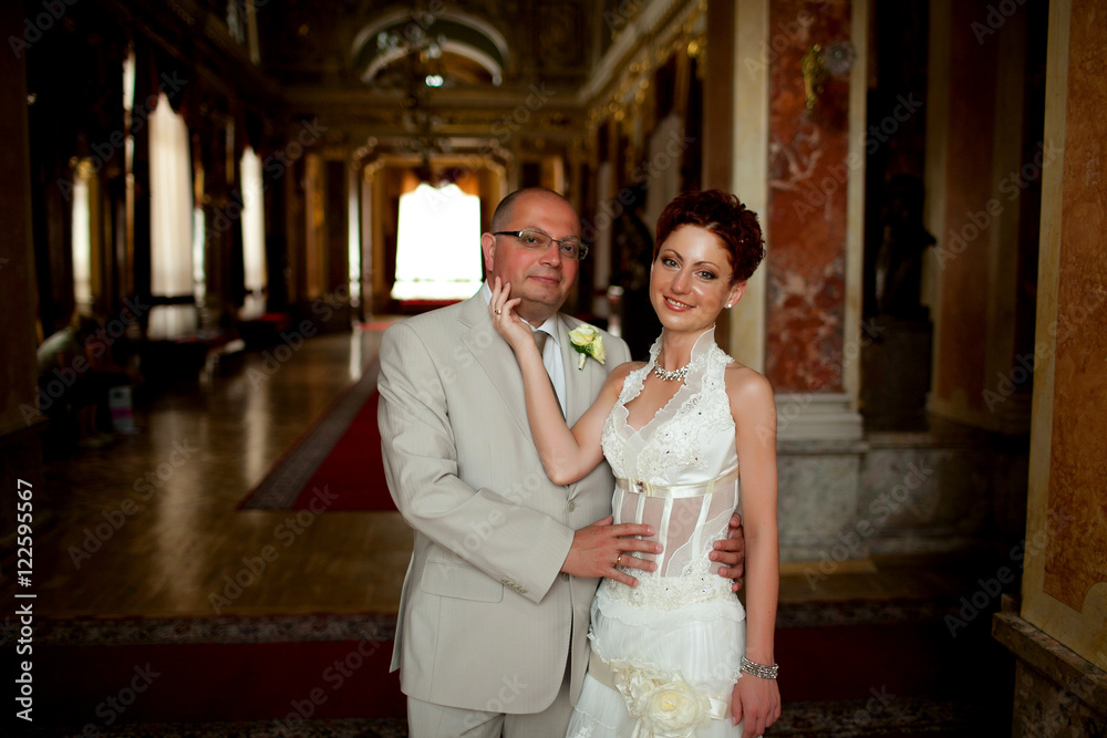Fototapeta premium Short-haired bride strokes groom's chin while they pose in old r