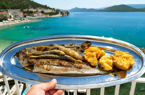 A plate of grilled fish and a beautiful view of the blue sea