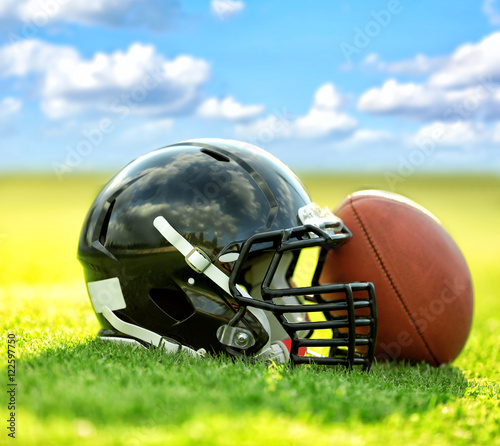 Rugby helmet with ball on green grass and blue sky background