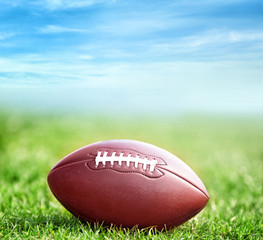 American football ball on green grass and blue sky background