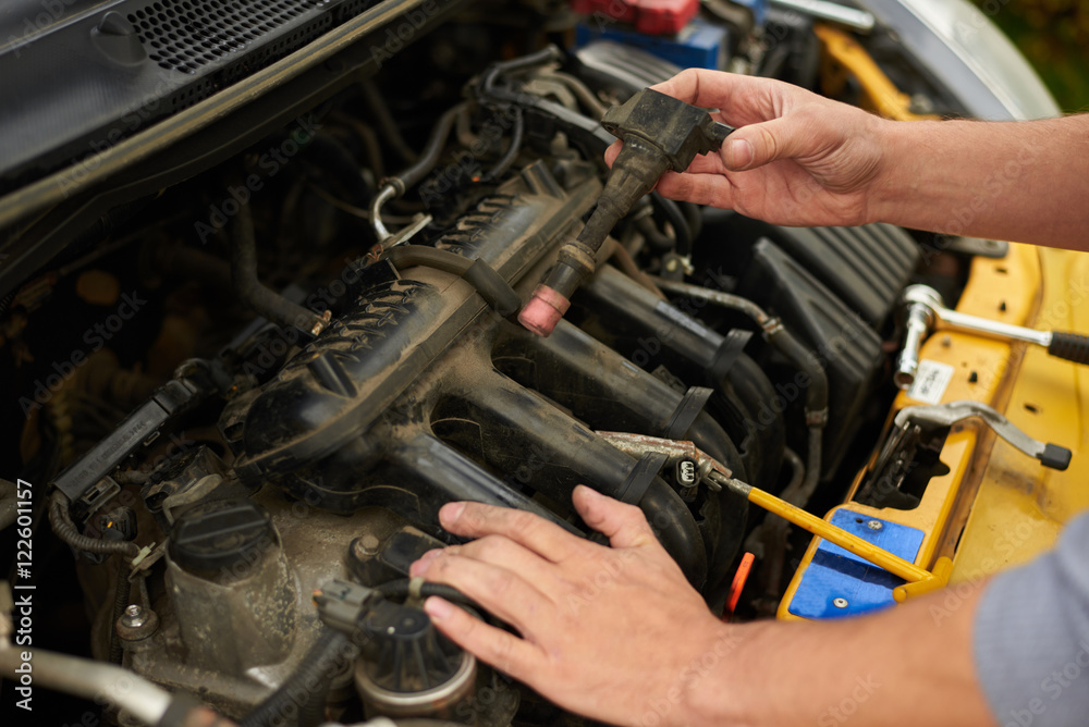 Man change spark plugs outdoor on yellow car Man change spark plugs outdoor on yellow car