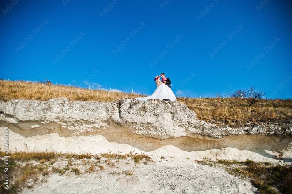 Charming bride in a wreath and elegant groom on landscapes of mountains, water and blue sky at sunny weather