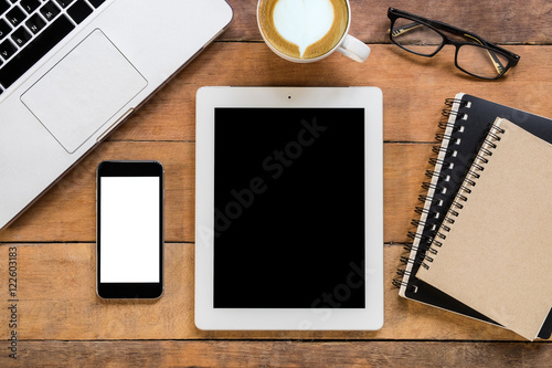 Office stuff with blank screen smartphone, blank screen tablet, laptop, leather notebook, glasses and cup of coffee. Top view with copy space.Office desk table concept.