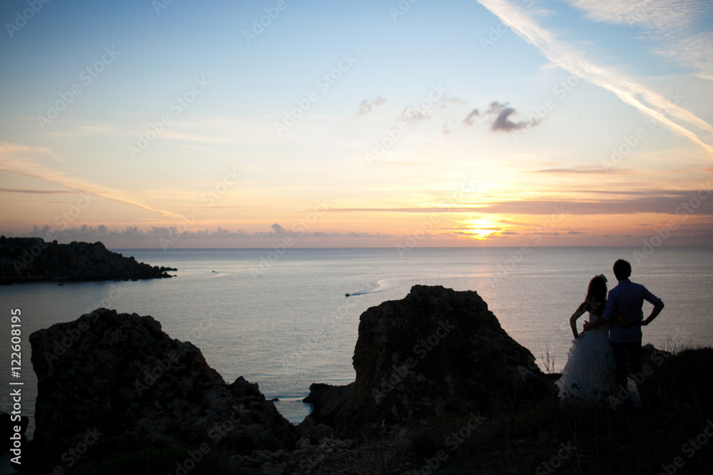 Silhouettes of lovely wedding couple watching the sunset over th