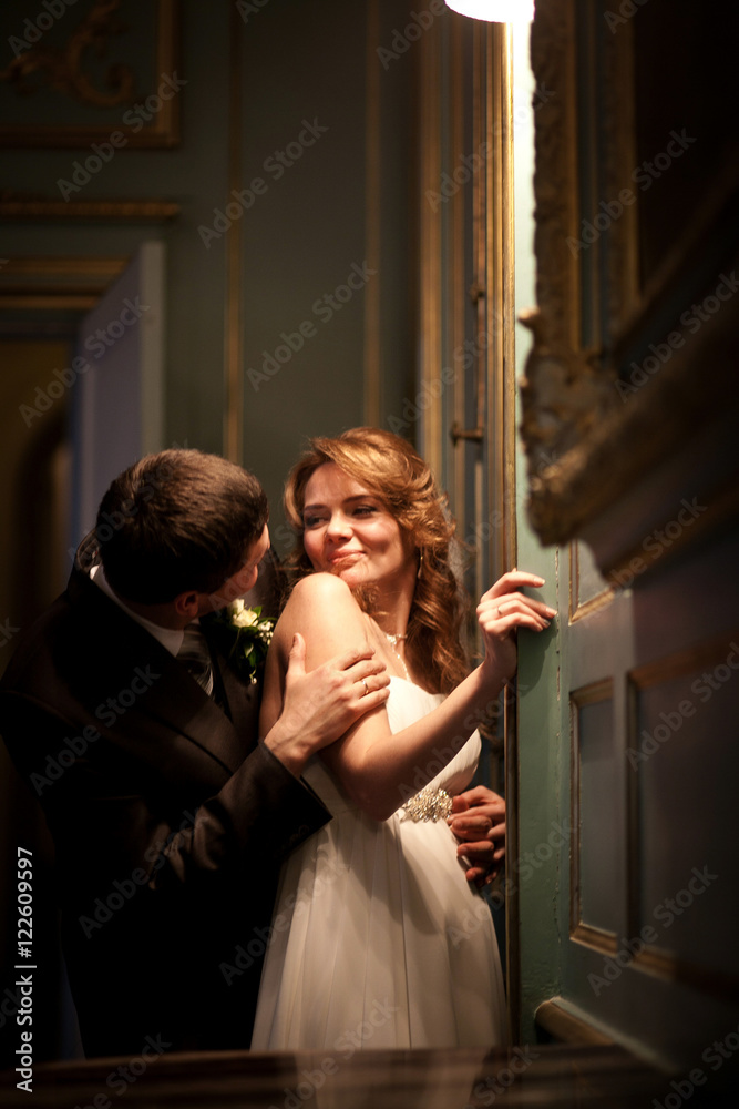 Bride looks at groom over her tender shoulder while he hides beh Bride looks at groom over her tender shoulder while he hides beh