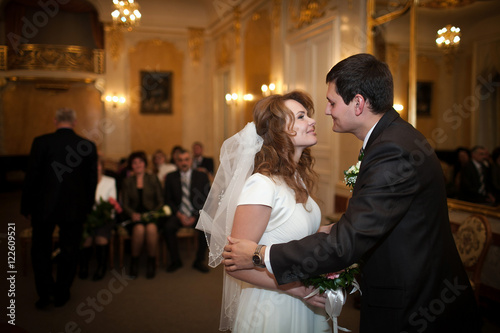 Groom leans to bride for a kiss while they stand in the hall ful