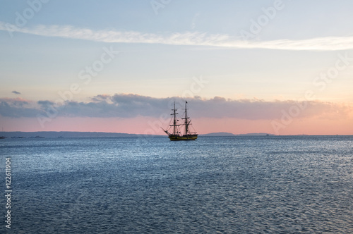 sailing ship at anchor, a blue calm sea and cloudless sky