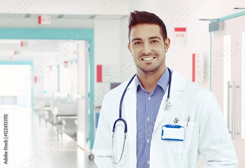 Happy young physician standing at hospital hallway