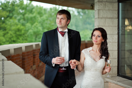 Groom in black tuxedo holds bride's hand while they walk along t photo