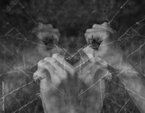 Lots of tortured hands grasping desperately barbed wire on black and white background