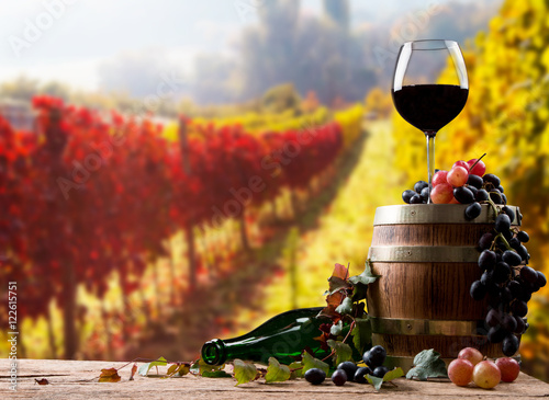 Red wine bottle and wine glass on wooden barrel with nature background