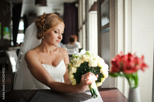 Blonde bride looks at her wedding bouquet while resting at the t