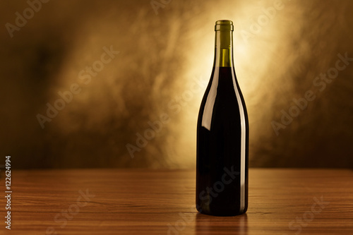 Red wine bottle on wooden table and golden background