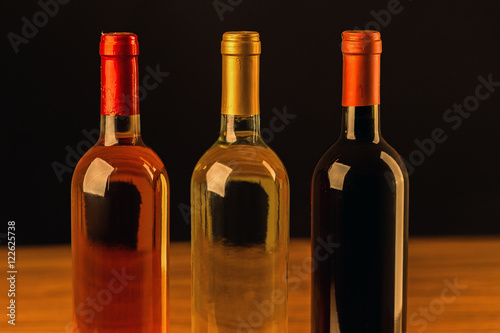 Rose, white and red wine bottles on wooden table and black background