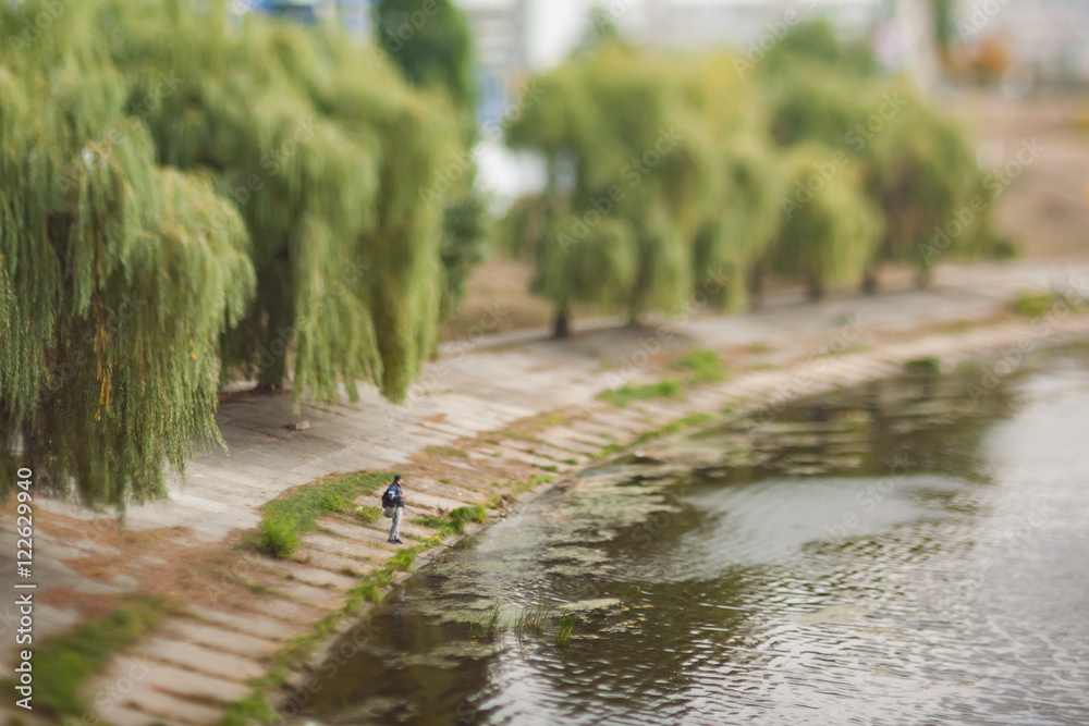The man is fishing on the canal. Soft and blurry cityscape. Natural optical tilt shift photo.