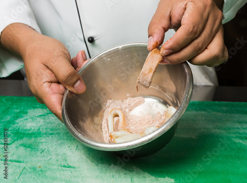 Raw calamari rings being placed into a metal mixing bowl with mexican spices