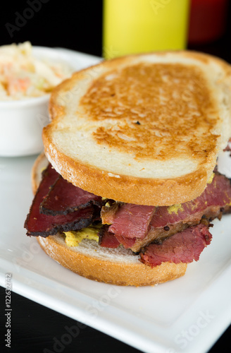Smoked meat beef sandwich with mustard and black pepper corns, served on a plate with coleslaw.
