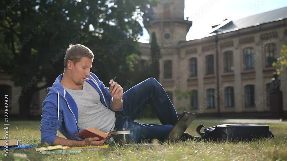 Handsome focused student studying on campus lawn Handsome focused student studying on campus lawn