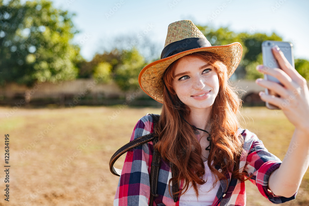 Smiling woman cowgirl taking selfie with mobile phone on ranch