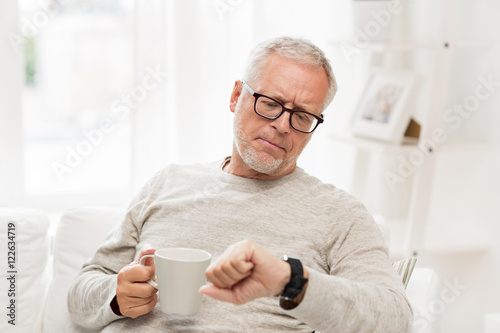 senior man with coffee looking at wristwatch