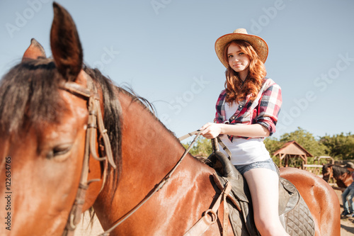 Happy redhead young woman cowgirl smiling and riding horse