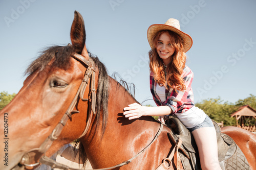 Happy pretty young woman cowgirl riding horse