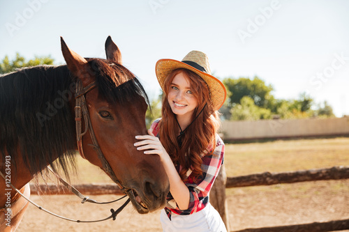 Smiling beautiful young woman cowgirl with her horse on farm