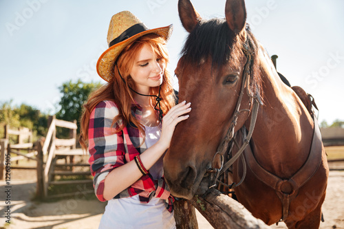 Smiling tender young woman cowgirl with her horse on ranch