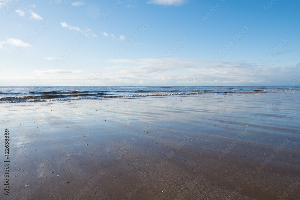 relaxing and gentle calming waves flowing into a beach at sundown, with a vivid blue sky and reflection