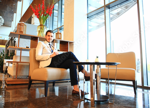happy young businessman sitting on sofa in hotel lobby
