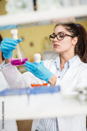 Young female scientist in lab coat wearing gloves  doing experiments in lab.