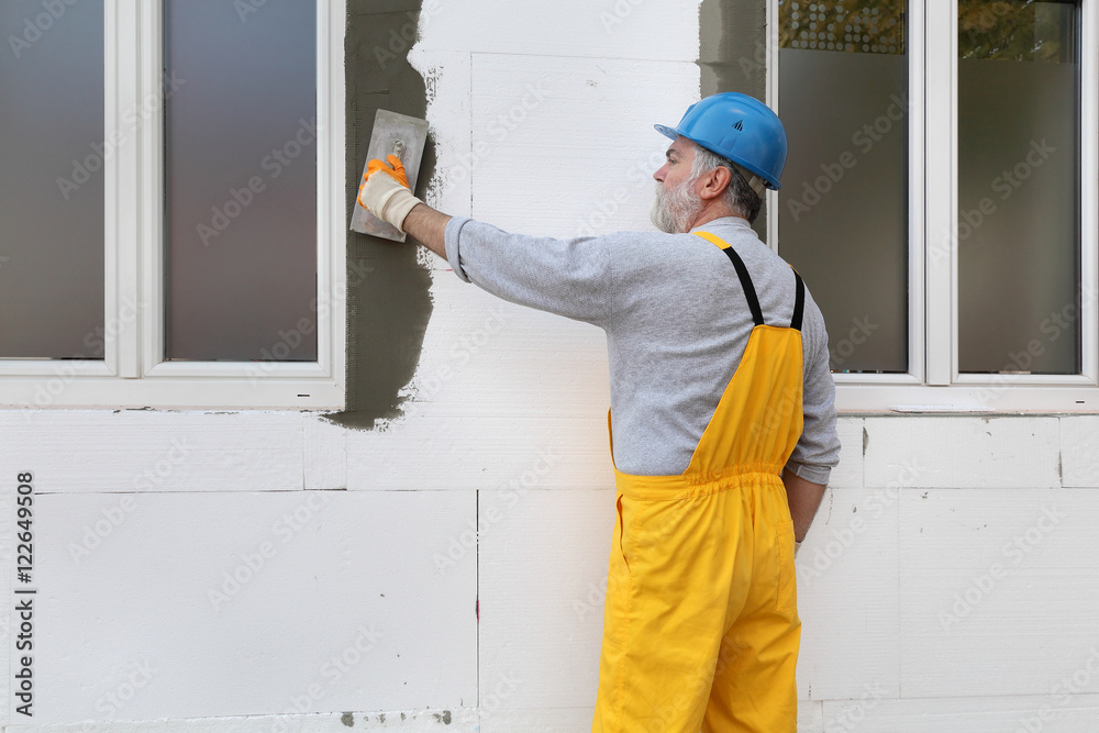 Worker spreading mortar over styrofoam wall insulation with trowel Worker spreading mortar over styrofoam wall insulation with trowel