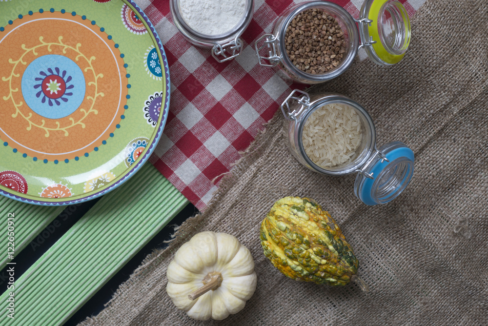Pumpkin, jars with flour, buckwheat and rice, colored plate on a wooden table. Pumpkin, jars with flour, buckwheat and rice, colored plate on a wooden table.